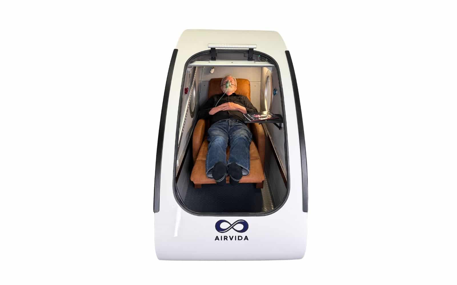 Patient reclining comfortably inside an Airvida hyperbaric oxygen chamber with eyes closed during a mental health HBOT session.