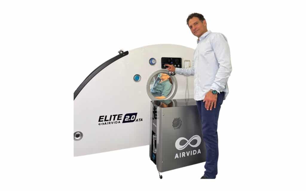 Dr. Adam Fields operating the control panel of an Airvida Elite 2.0 ATA hyperbaric oxygen chamber with a patient inside.